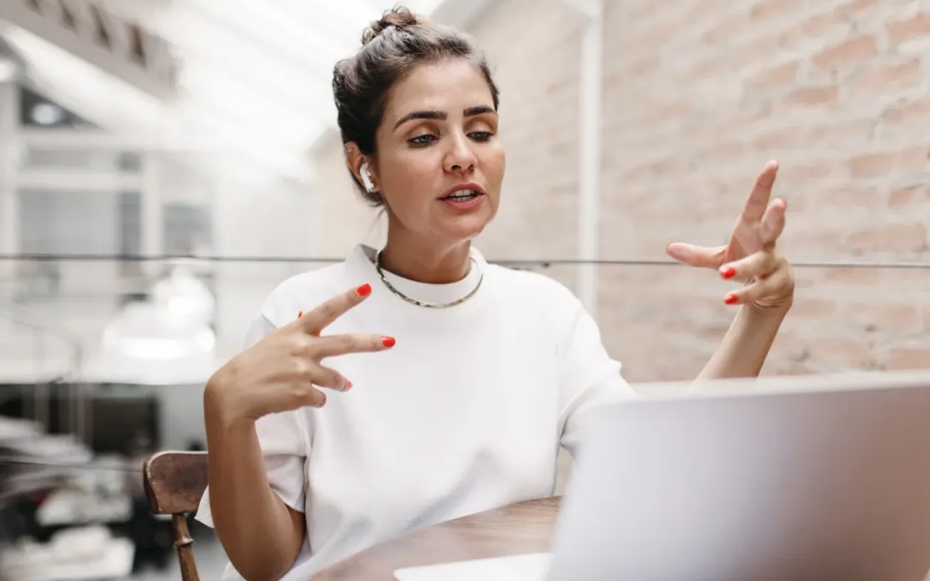 Woman sitting in front of a laptop with headphones in ear, engaged in conversation