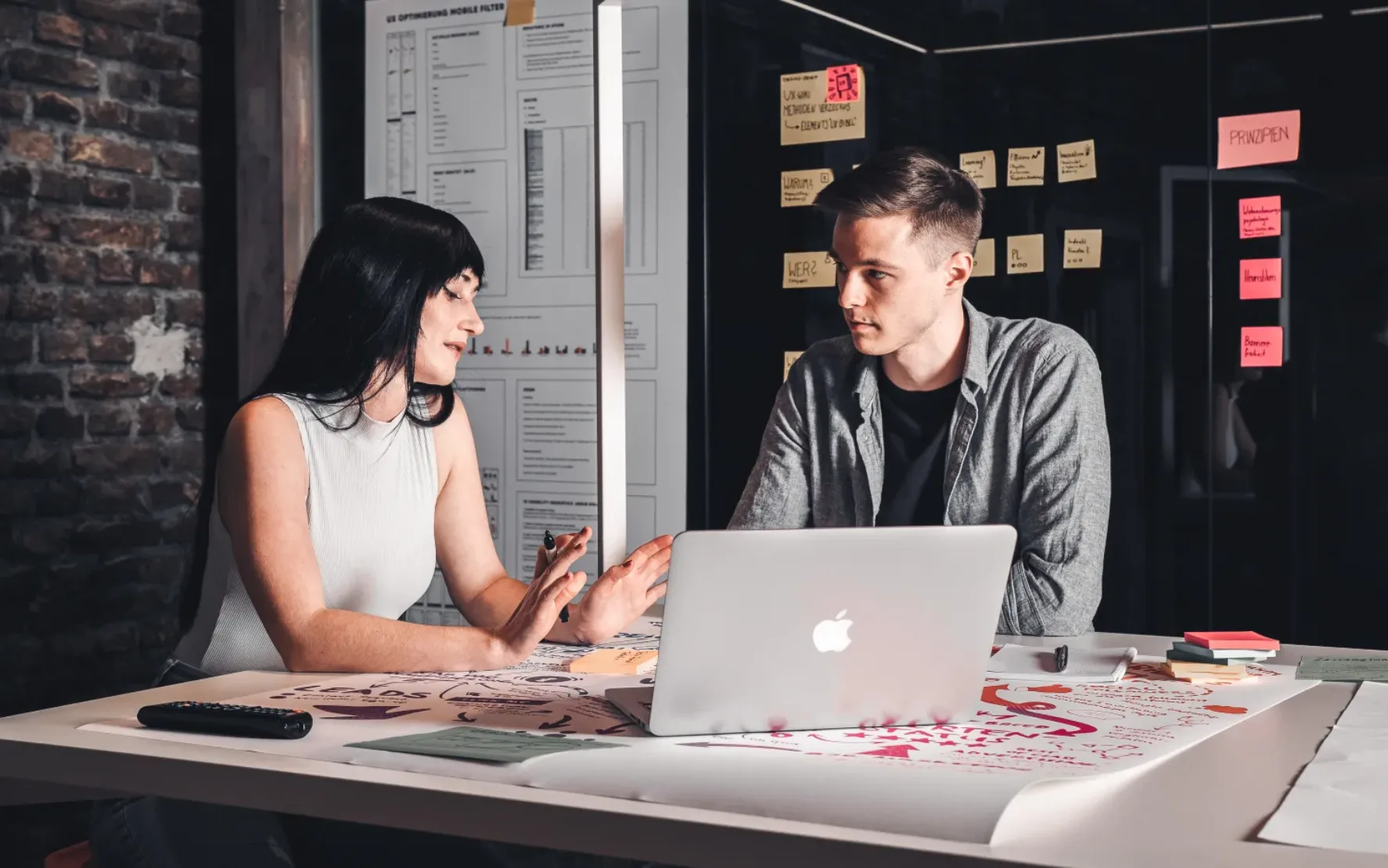 Foto von zwei Grafikdesigner*innen, die vor einem Laptop sitzen und über ein Websitedesign sprechen.