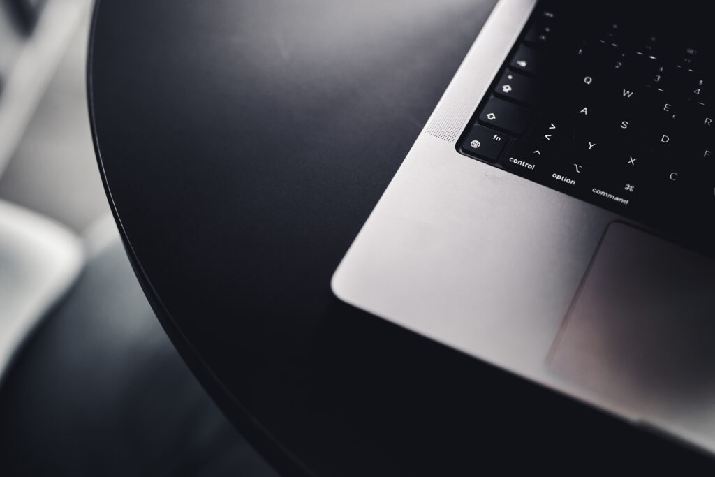 Bildausschnitt von einem silbernen Laptop auf einem schwarzen Tisch.