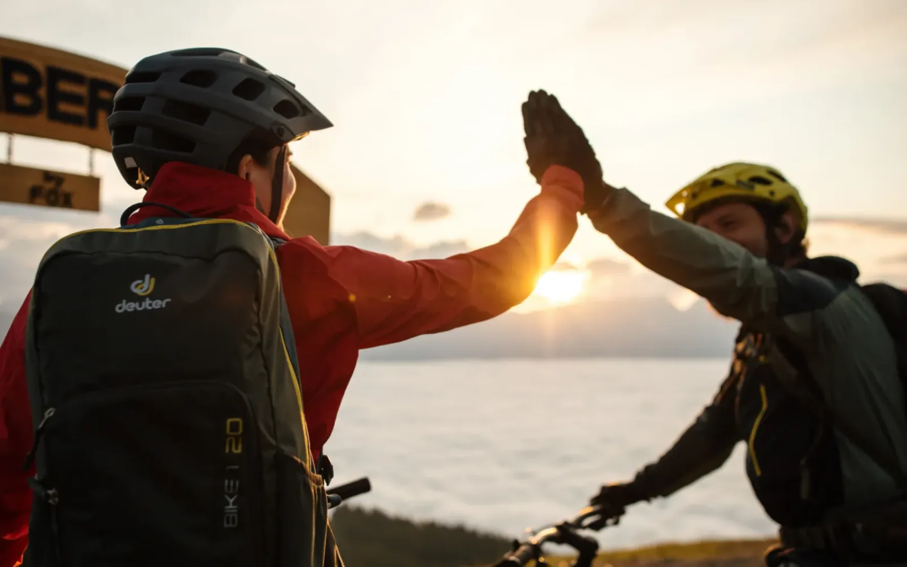 Zwei Mountain-Bike-Fahrer, die sich gerade High-Five geben - im Hintergrund sieht man den Sonnenuntergang.