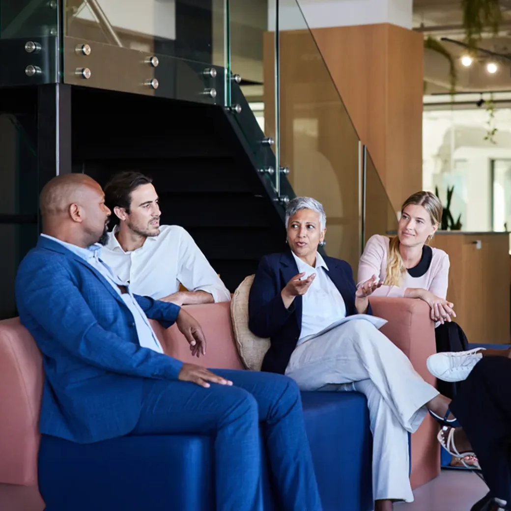 Diverse group of smiling businesspeople talking together during a casual meeting in the lounge area of a modern office