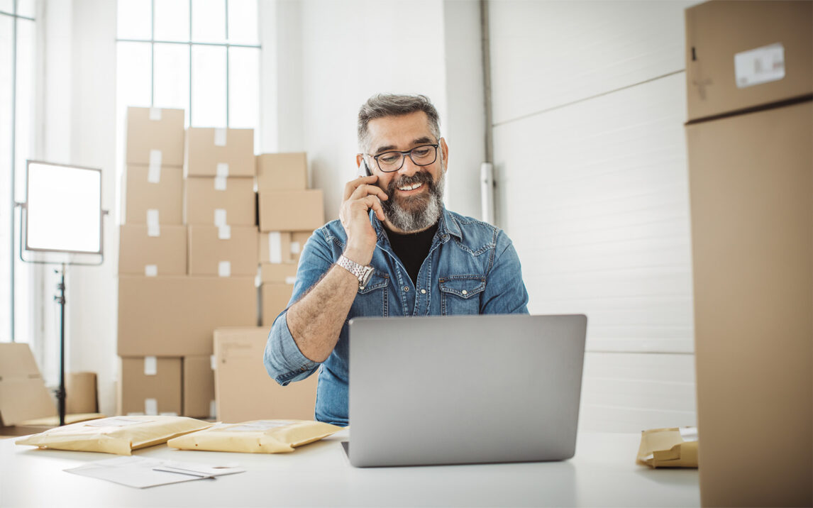 Bearded men working on packaging and online delivery in home office business. He talking on phone with customer