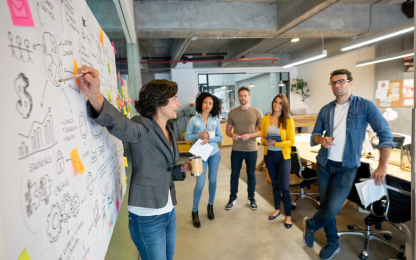 Woman making a business presentation in a meeting at a creative office and pointing to her team her business plan