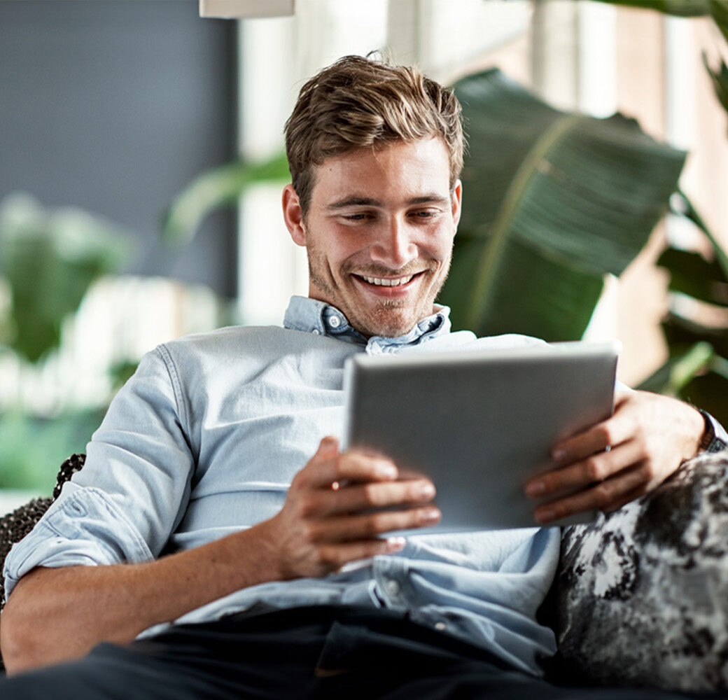 Shot of a happy young man using his tablet while relaxing on the couch at home