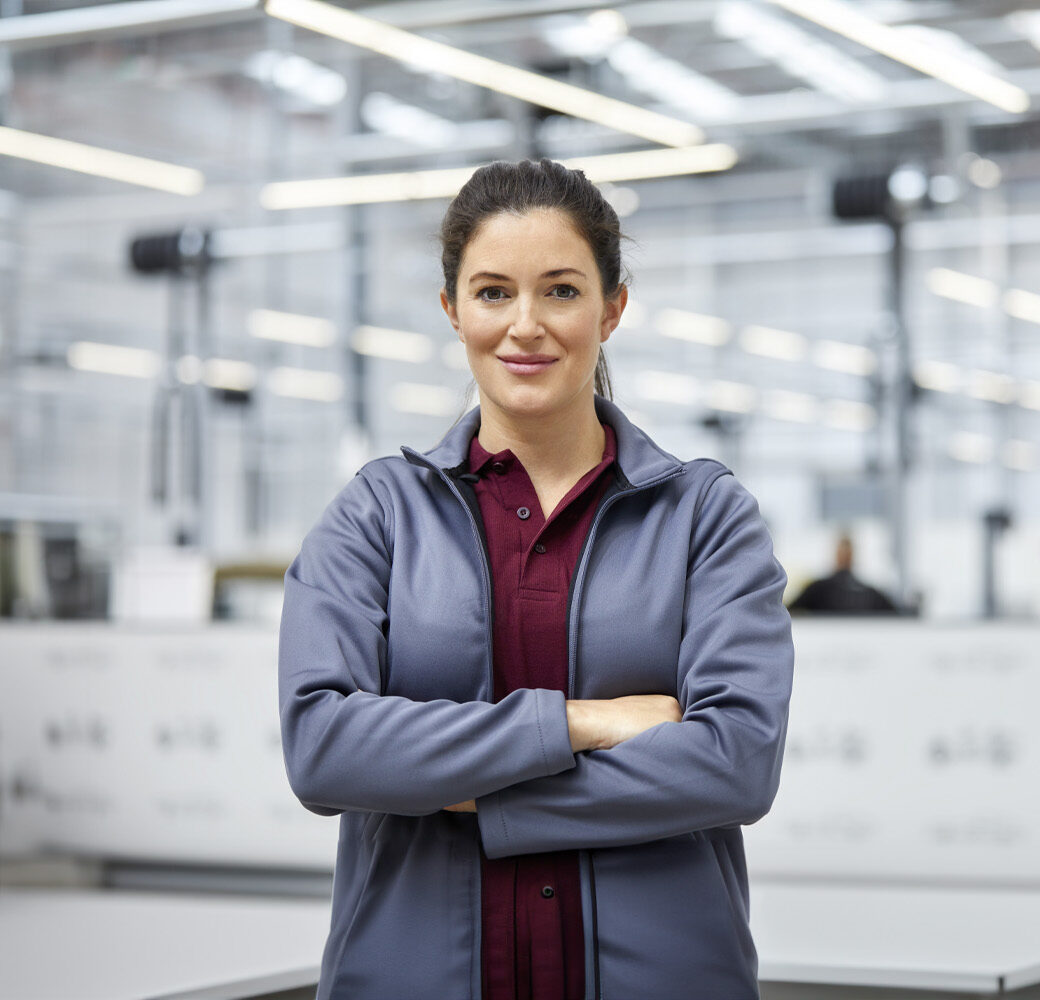 Portrait of female engineer with arms crossed in automobile industry. Confident technologist is standing in showroom. She is in jacket at factory.