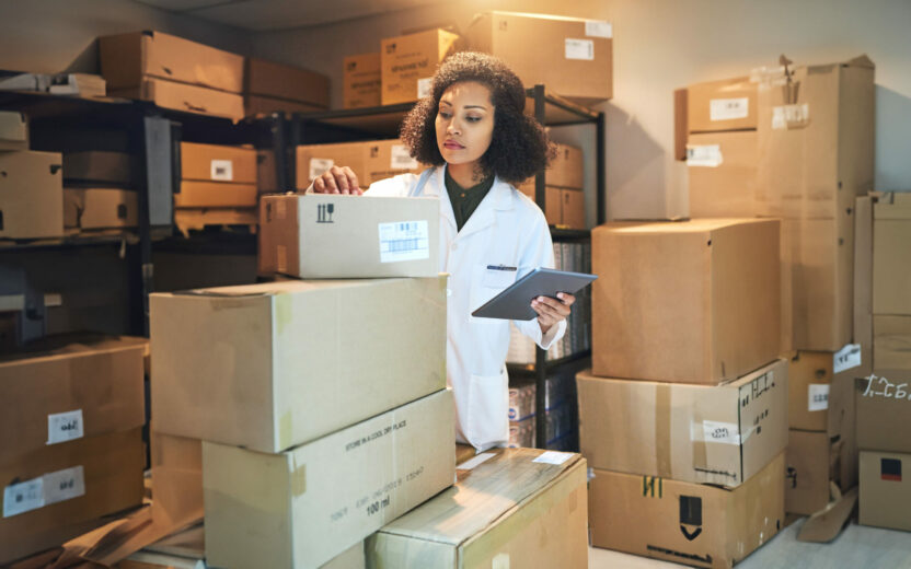 Photo of a young woman using a digital tablet while taking stock in the storeroom of a pharmacy