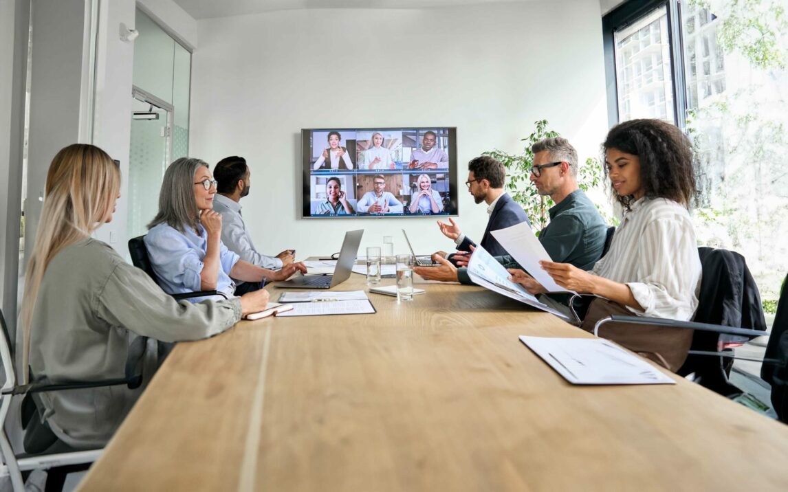 Diverse company employees having online business conference video call on tv screen monitor in board meeting room. Videoconference presentation, global virtual group corporate training concept.