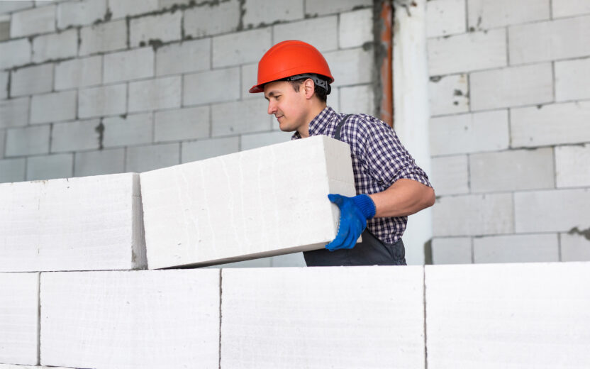 Man wearing a red helmet working, building a wall from bricks.