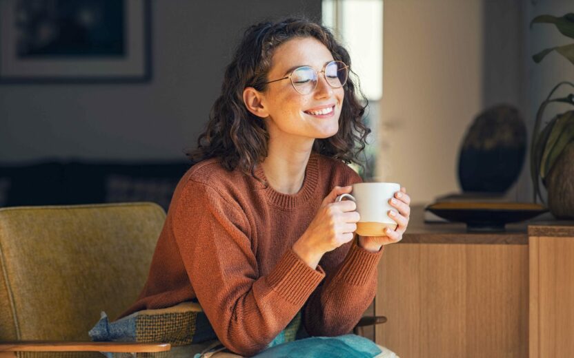 Happy young woman drinking a cup of tea or coffee in an autumn morning.