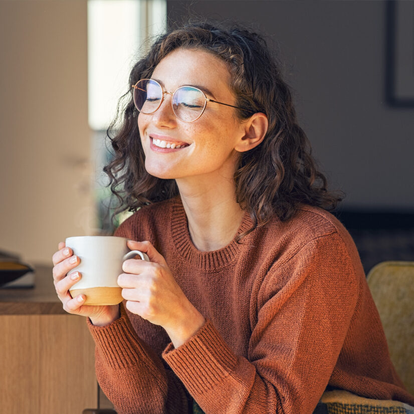 Happy young woman drinking a cup of tea or coffee in an autumn morning.