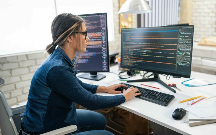 Female developer coding and programming. Coding on two with screens with code language and application.