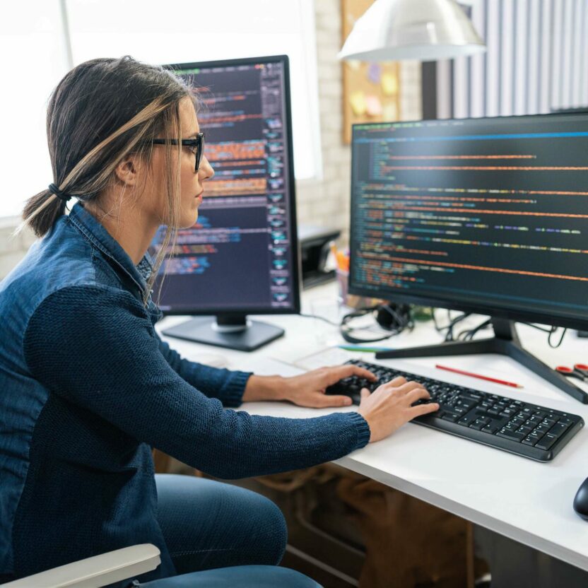 Female developer coding and programming. Coding on two with screens with code language and application.