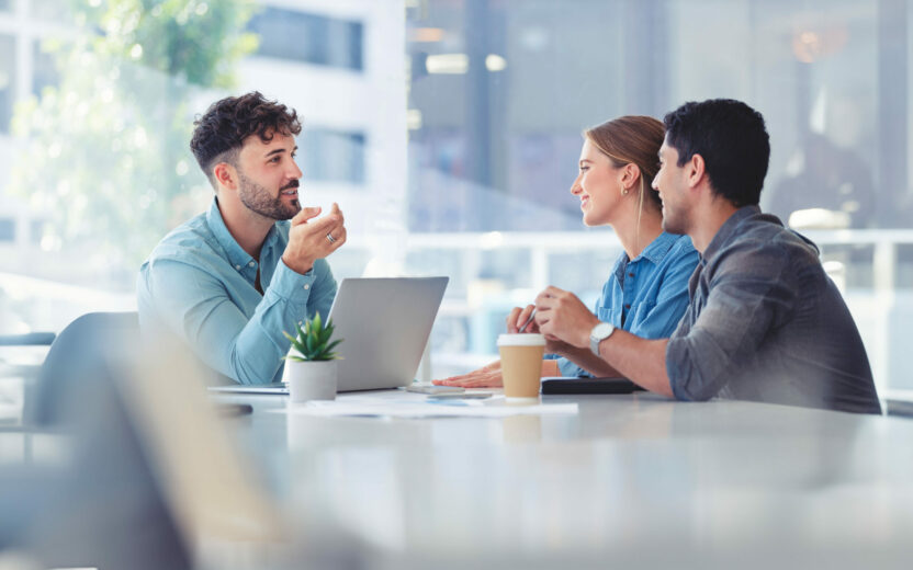 People in a meeting, financial advisor with couple explaining options. The agent is using a computer. Couple are casually dressed. They sitting in an office and are discussing something with the agent.