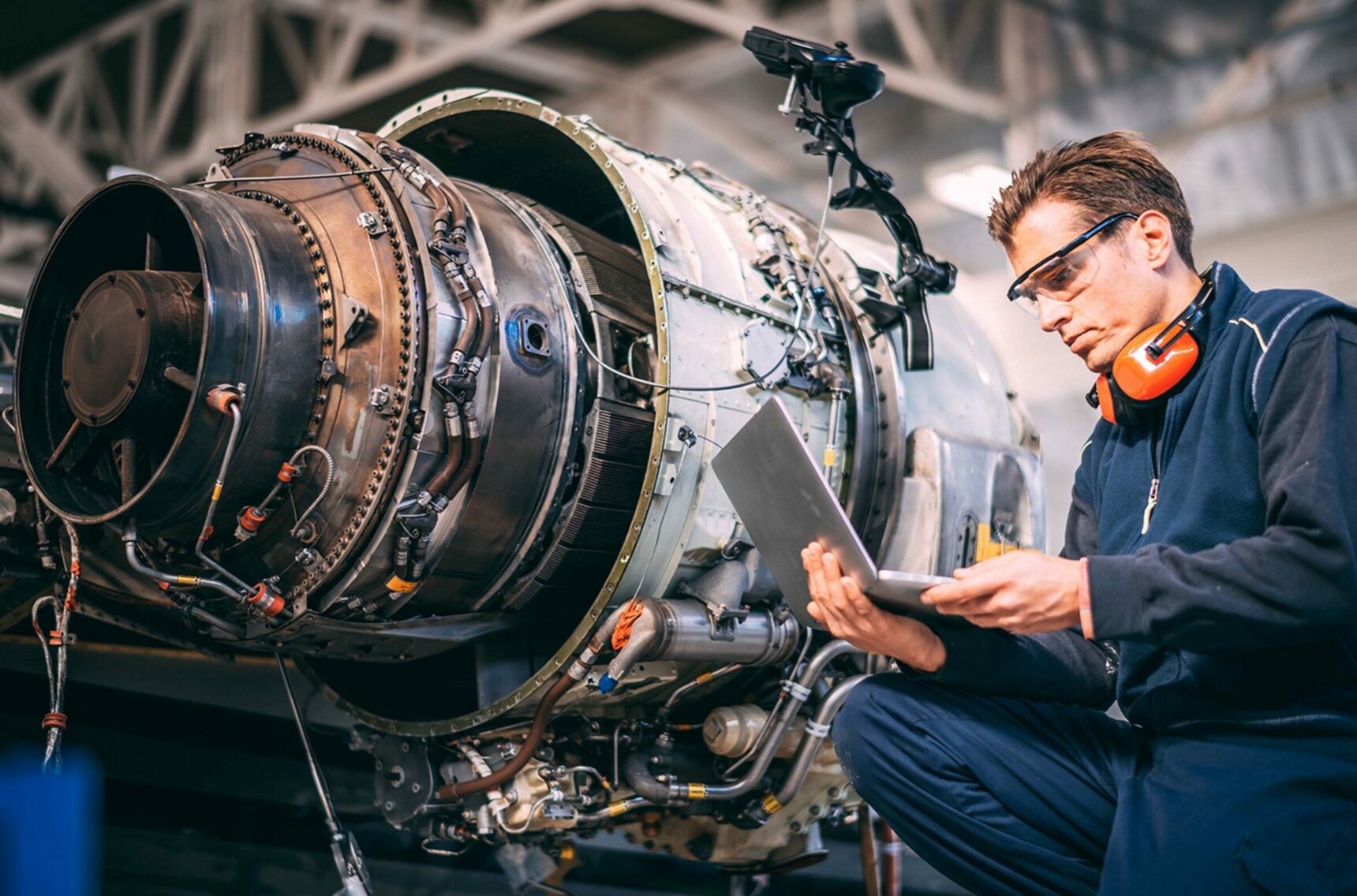 Aircraft engineer in a hangar using a laptop while repairing and maintaining an airplane jet engine