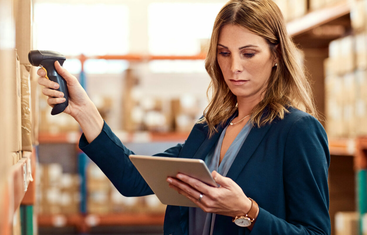 Woman scans goods in warehouse and looks at tablet | procurement record in SAP