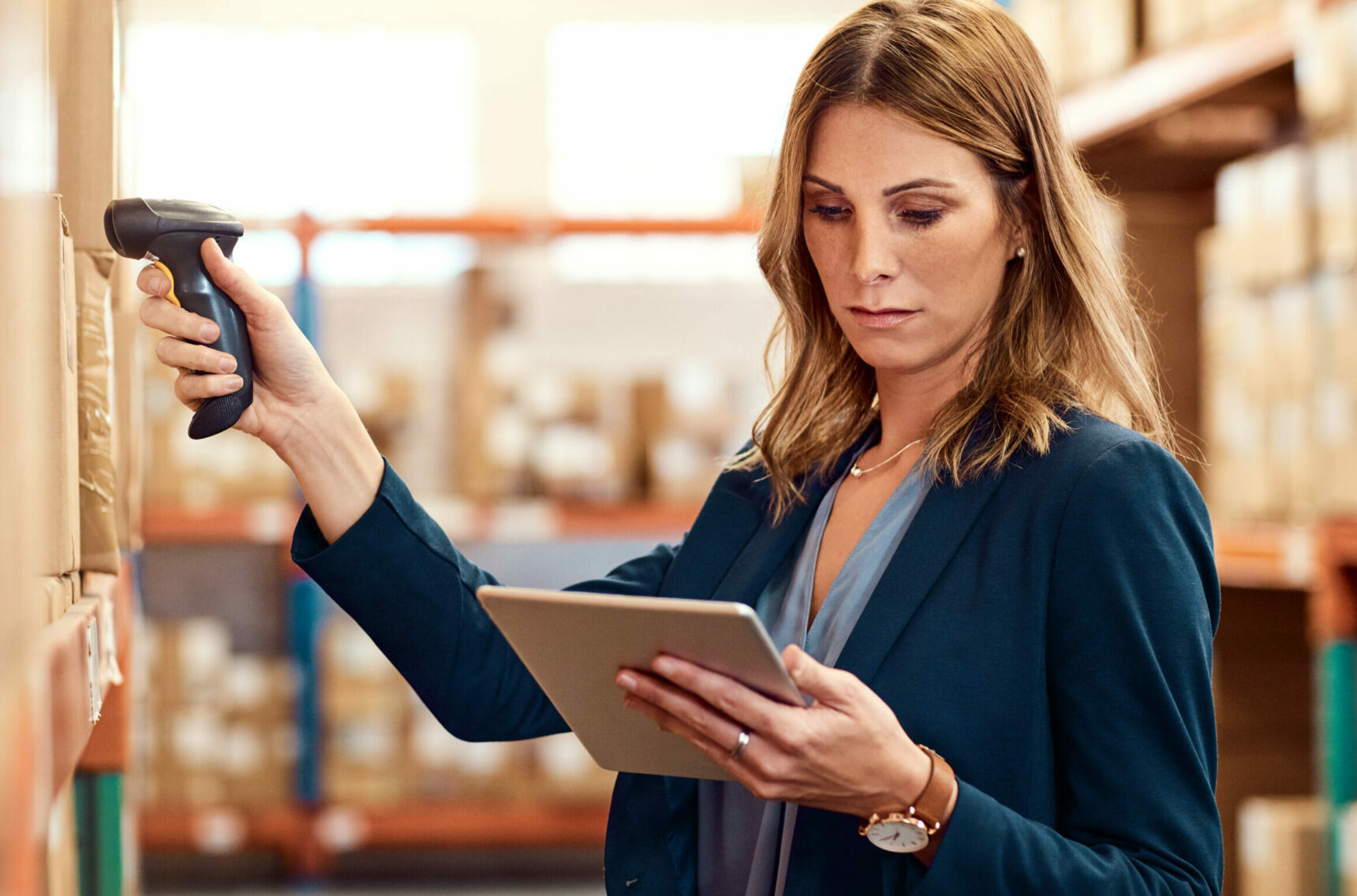 Woman scans goods in warehouse and looks at tablet | procurement record in SAP