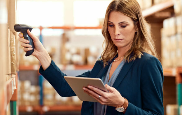 Woman scans goods in warehouse and looks at tablet | procurement record in SAP