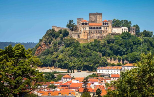 Main facade of the Castle of Leiria in Portugal, in full sunny day with blue sky, with some buildings at the base of its hill