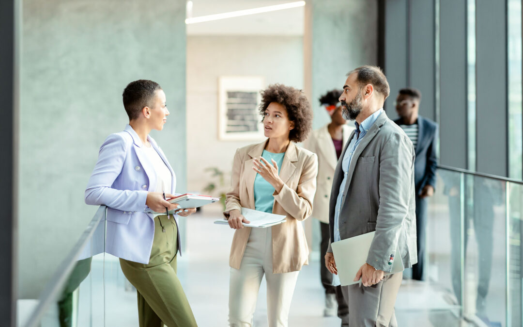 Diverse group of businesspeople discussing work while standing together in a bright modern office corridor