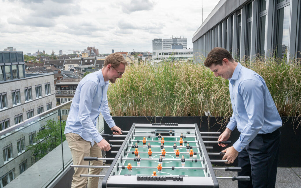 Zwei Consultants spielen Kicker auf Dachterrasse im valantic Büro Köln Rudolfplatz