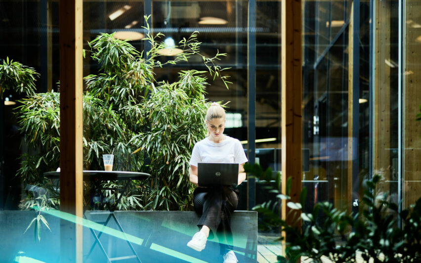 valantic CX Mitarbeiterin, die in einem begrünten Wintergarten am Laptop arbeitet.