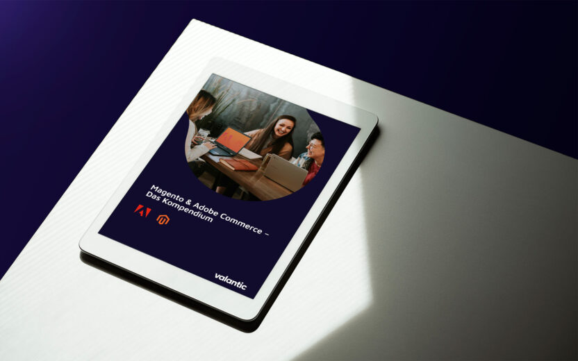 Auf einem iPad wird ein Dokument mit dem Titel „Magento & Adobe Commerce – Das Kompendium“ auf einer hellen Oberfläche mit dunklem Hintergrund angezeigt. Das Dokumentcover enthält ein Gruppenfoto sowie Logos von Adobe und Magento.