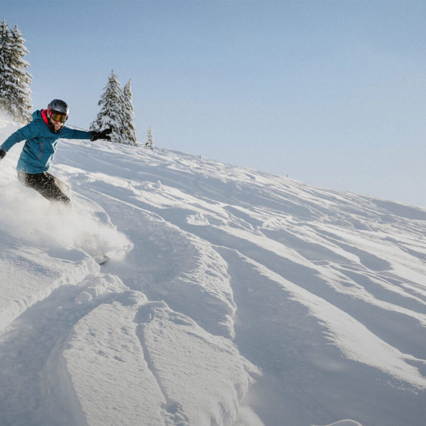 Headerbild für Adelboden-Lenk: Eine Person fährt auf einem Snowboard durch den Tiefschnee.