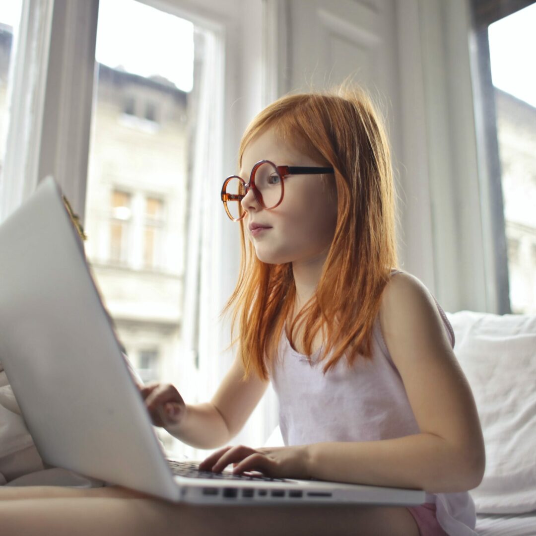 Ein junges rothaariges Mädchen sitzt und hat einen Laptop auf ihrem Schoß.