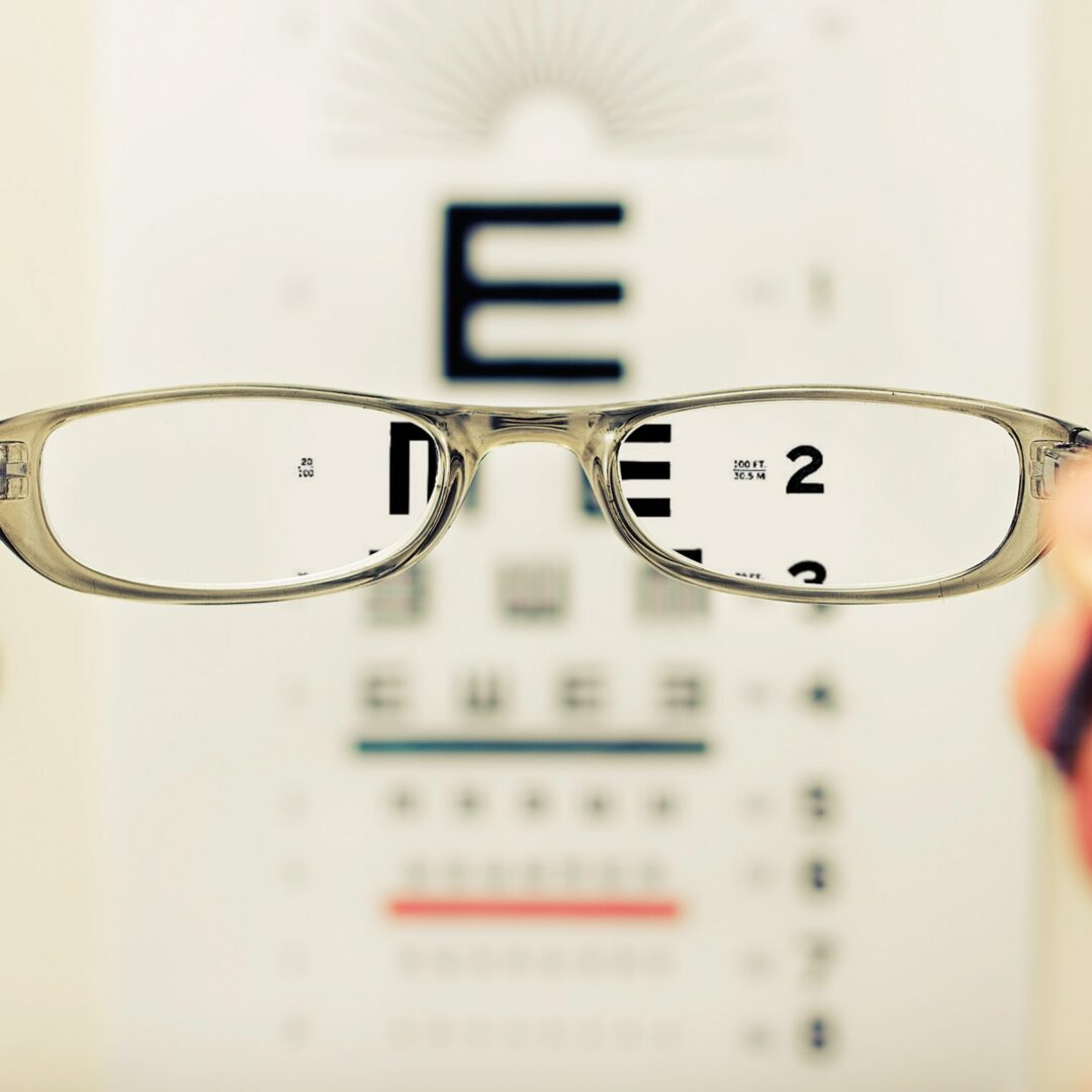 Eine Brille wird vor einem Sehtest-Textdokument gehalten, wodurch der Text durch die Gläser scharf und außerhalb der Gläser unscharf erscheint.