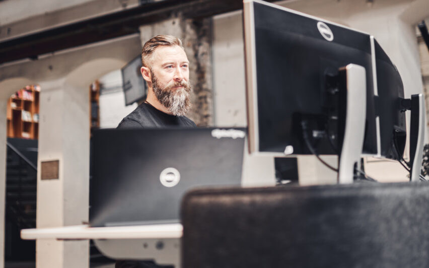 Mitarbeiter von valantic Austria an einem Steharbeitsplatz vor zwei Bildschirmen und einem Laptop