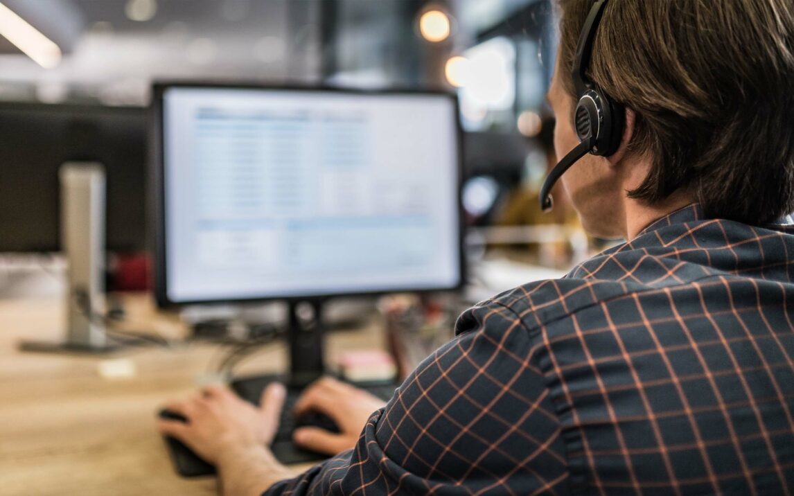 Person wearing a headset works on a computer in an office, facing the screen, which displays data.