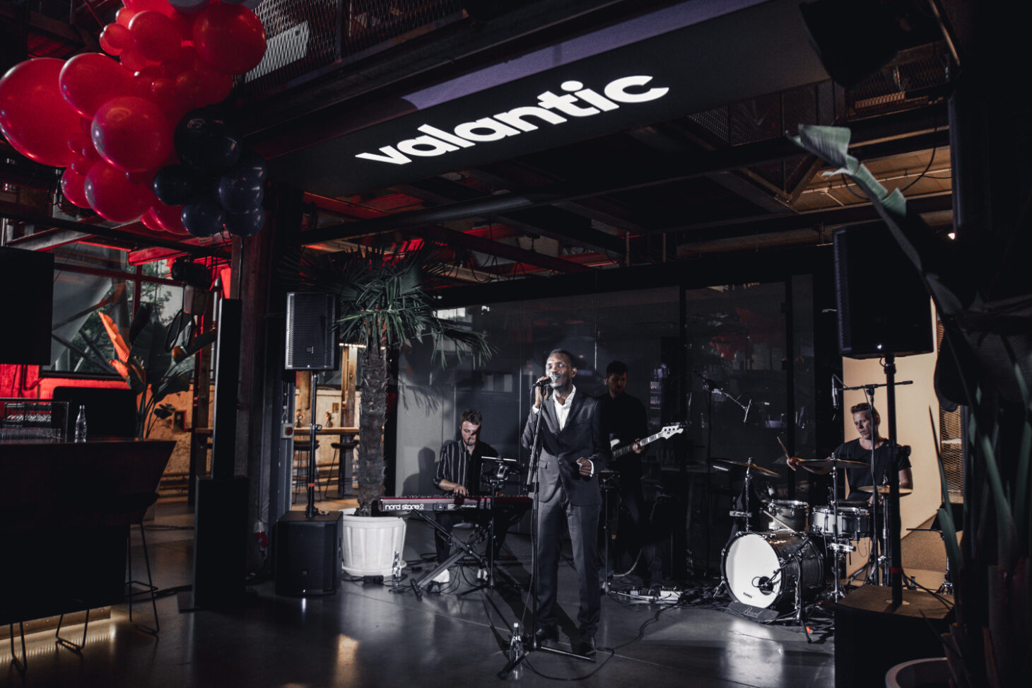 Eine Blues-Rockband spielt auf einer Partylocation im Industrial Style - über ihnen leuchtet das valantic-Logo