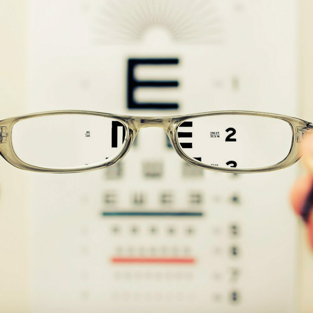 Glasses are held in front of a vision test text document, making the text appear sharp through the glasses and blurry outside of them.