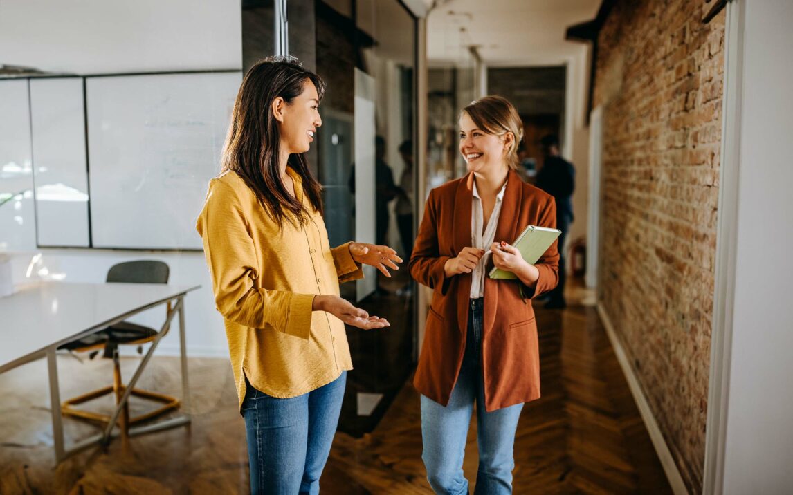 Two female colleagues talking in a hallway of modern office