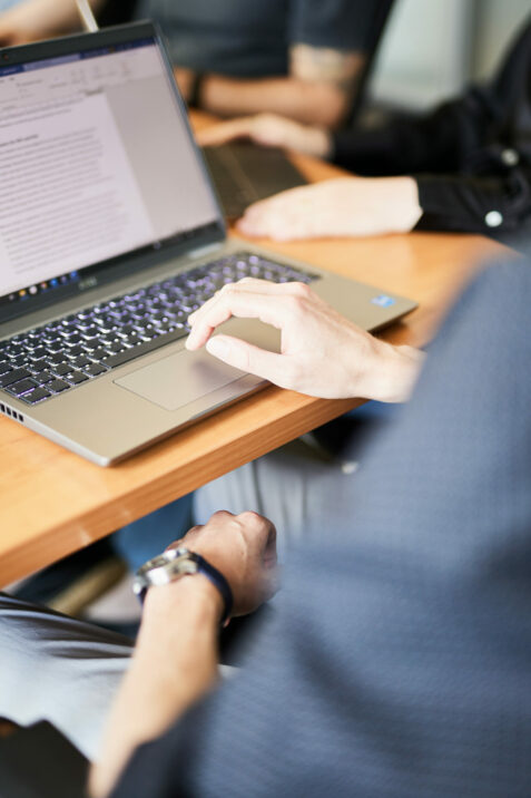 Image of a laptop on a conference table with someone's hand resting on the keyboard.