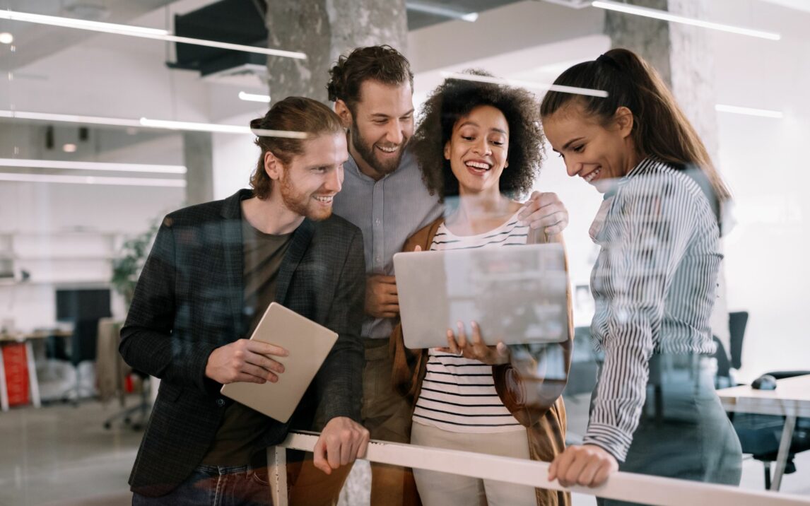 A group of people working together and looking at a tablet with joy on their faces.