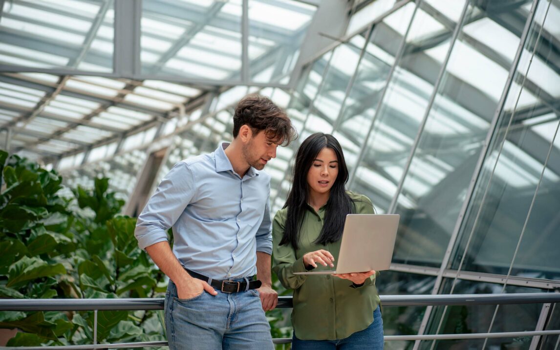 Businesswoman sharing laptop with colleague working in corridor