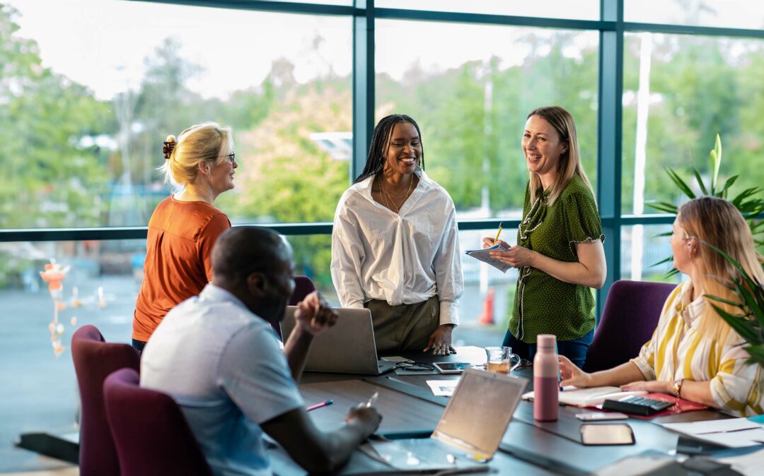 An over-the-shoulder view of a group of cheerful co-workers having a team briefing and enjoying some time away from their desks and recounting funny stories from the office.