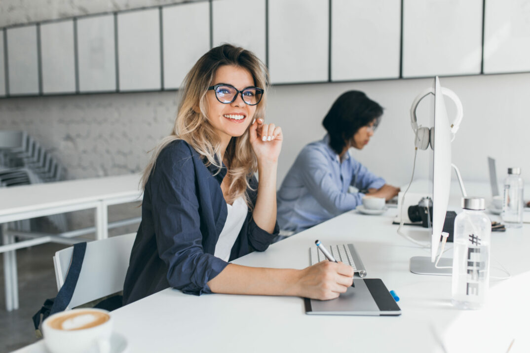 Beautiful female office worker carrying out administrative work for company. Indoor portrait of cute blonde student doing homework with asian universuty friend.