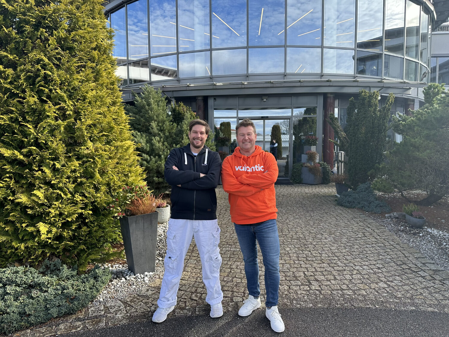 Alexander Mohr-Miesler and Marco Kahler standing with arms crossed in front of a contemporary glass building.