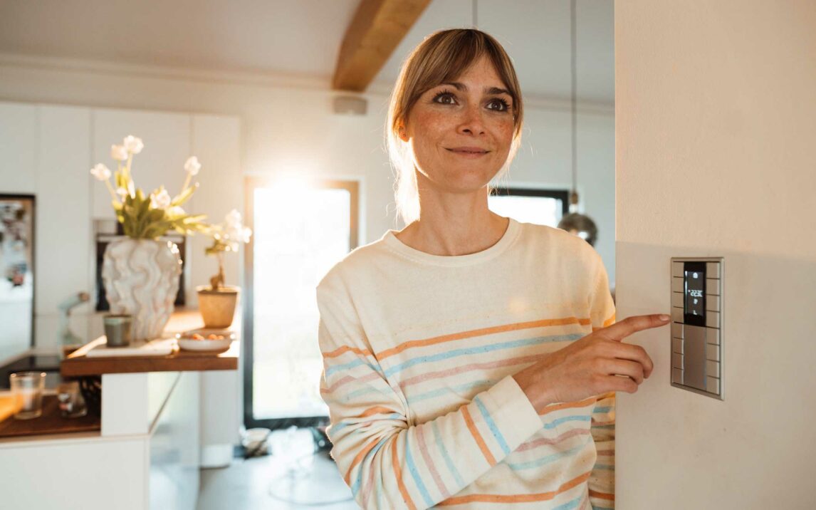 contemplative woman operating thermostat on wall