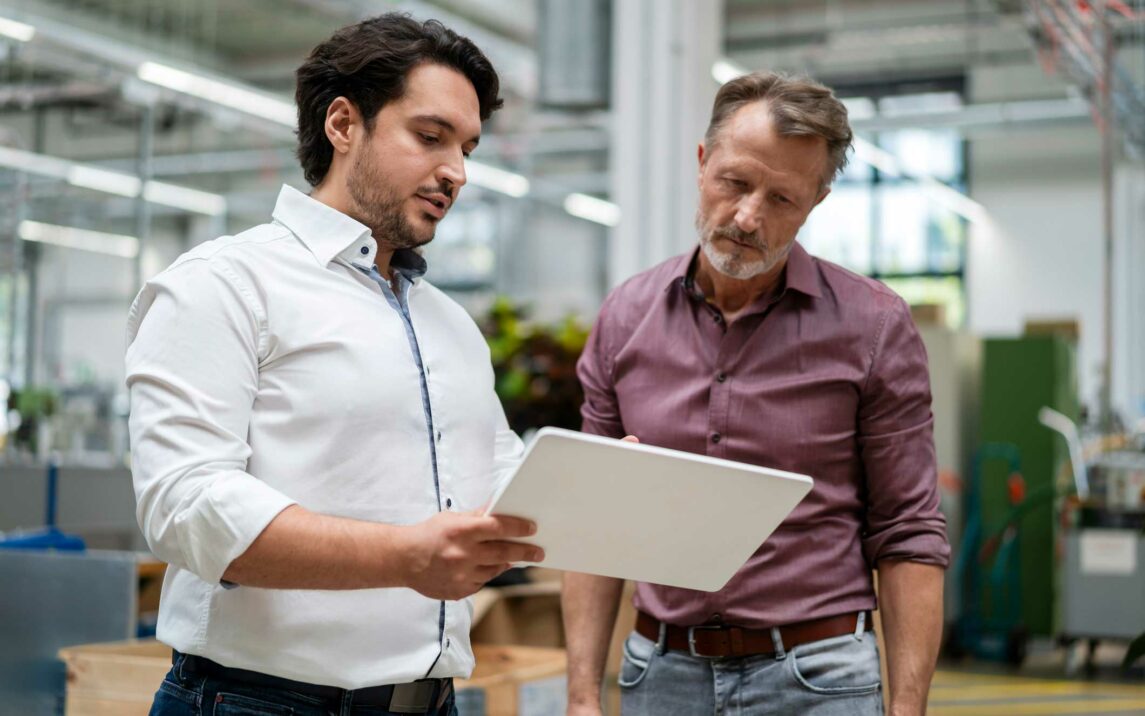 young businessman showing tablet pc to colleague at factory