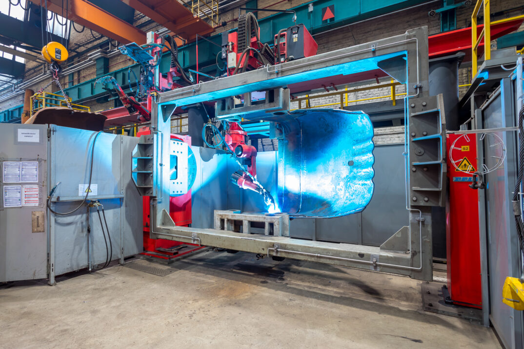 A robot arm welds metal in a production plant equipped with industrial machines and electronic control systems.