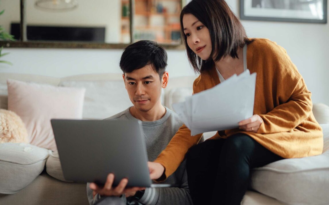 young couple discussing over financial bills while using laptop on sofa