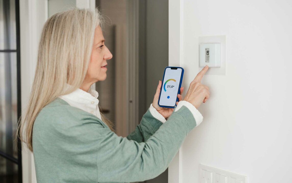 mature woman adjusting thermostat with smart phone