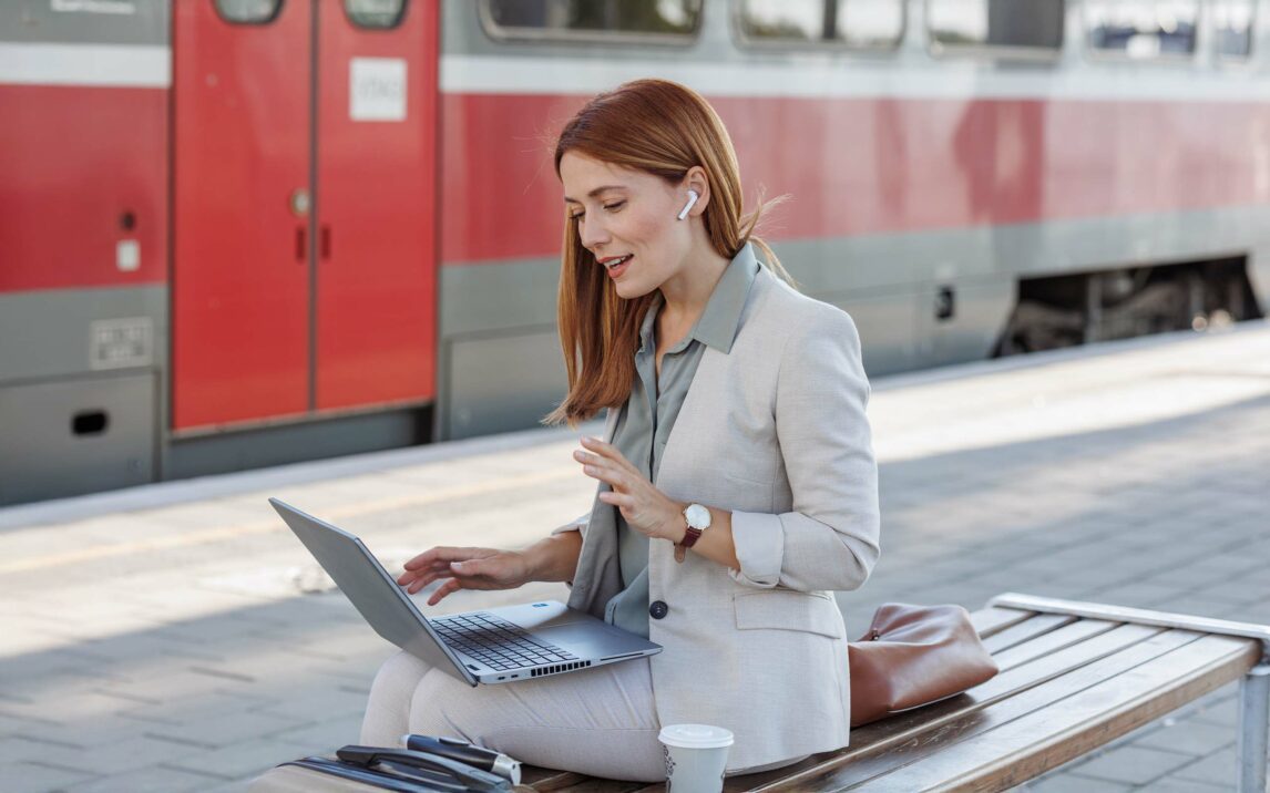 Businesswoman with in ear headphones using laptop at train station