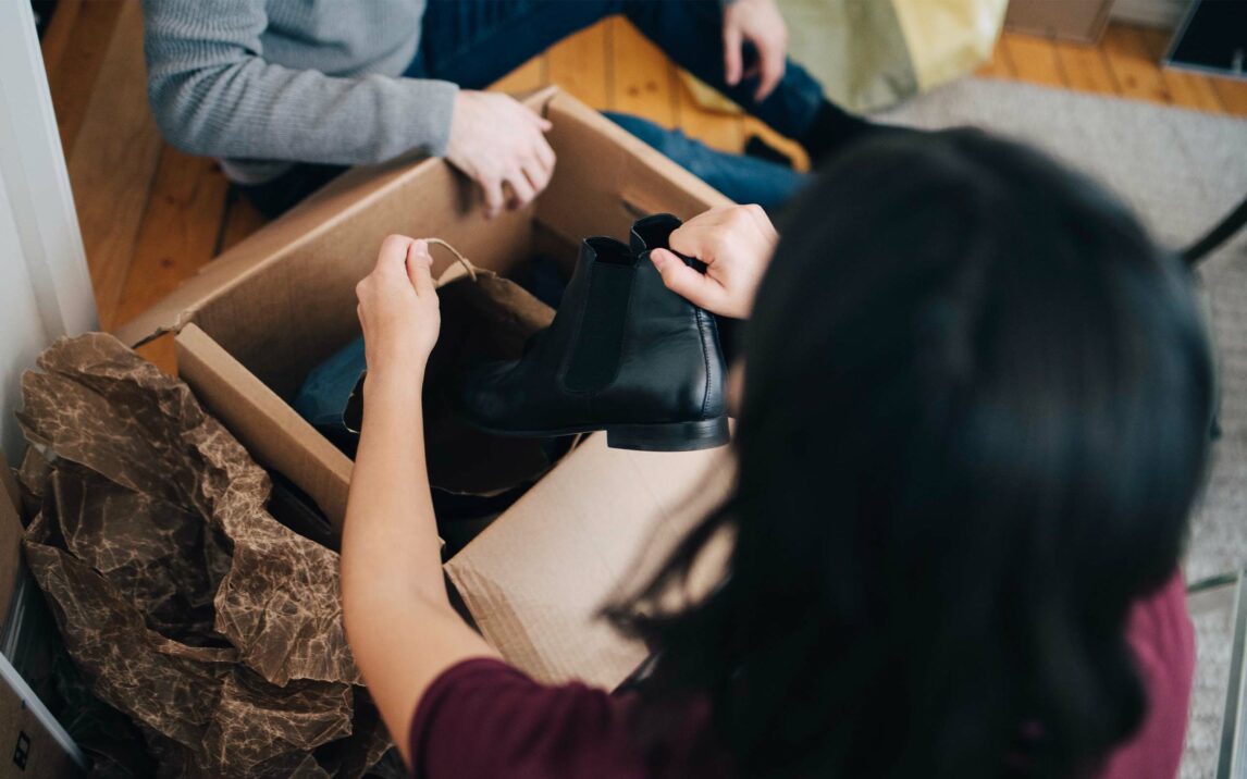 Woman removing shoe from box while sitting with man in apartment