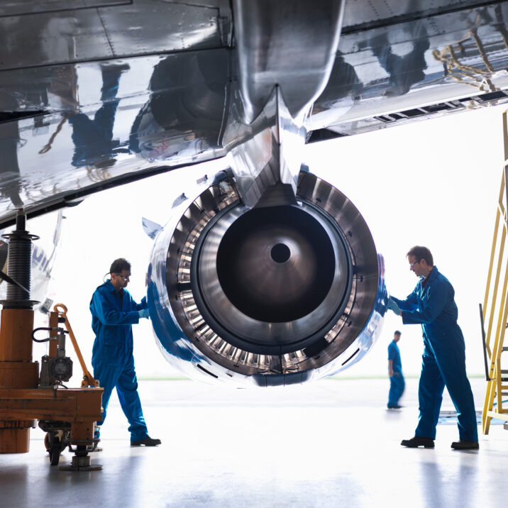 Foto von Ingenieuren, die an einem Flugzeugtriebwerk in einer Flugzeugwartungsfabrik arbeiten