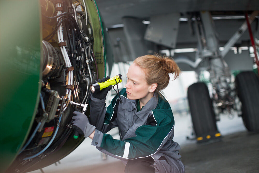 Foto von einem Ingenieur, der mit einer Taschenlampe ein Teil eines Flugzeugs analysiert