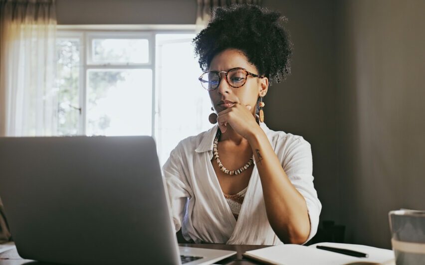 Woman thinking, planning, online research and brainstorming ideas on her laptop